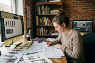 Jeune femme autodidacte en game design esquissant des wireframes de jeux vidéo à son bureau créatif fait maison